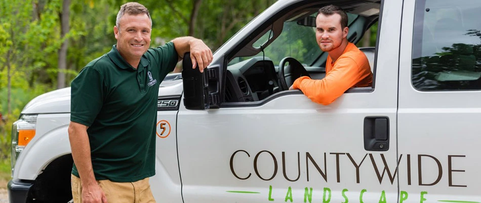 One of our landscapers leaning against one of our trucks with an employee sitting in the front seat on a job in Chester Springs, PA.
